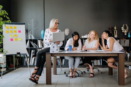 Free Four women collaborate in a modern office space, fostering teamwork and discussion. Stock Photo