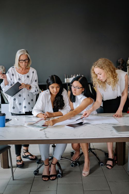 Free Four businesswomen collaborate in a modern office, discussing documents at a table. Stock Photo