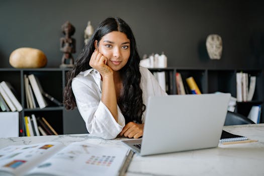 Young businesswoman in a white shirt working at a desk with a laptop, showcasing modern workplace ambiance.