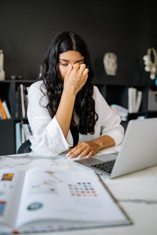 Free A woman feeling stressed while working on a laptop in an office setting with documents. Stock Photo