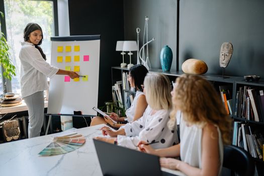 Group of women in a stylish office engaged in a creative planning session using sticky notes and a color palette.