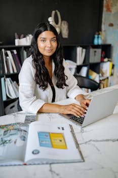Confident woman in modern office setting working on a laptop, embodying professionalism and focus.