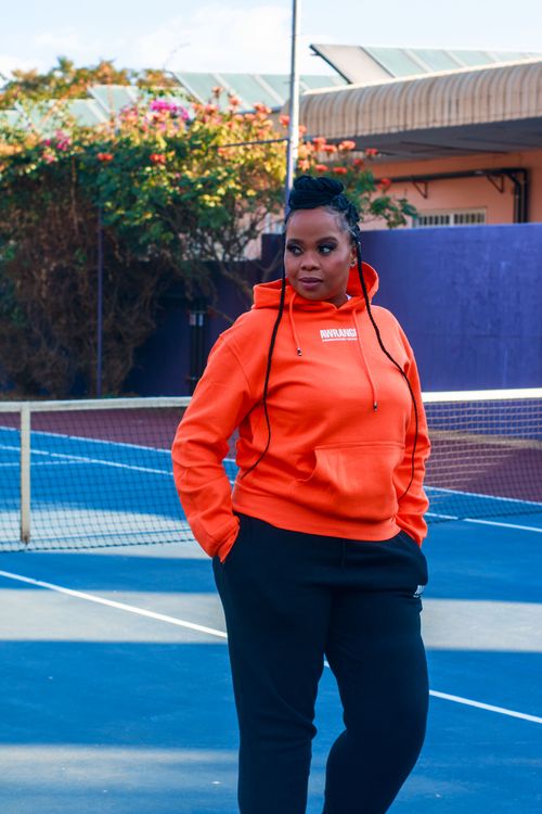 Free Fashionable woman in orange hoodie standing on tennis court, displaying urban street style Stock Photo