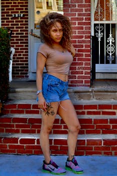 Woman in casual attire posing in front of a brick house, showcasing casual urban fashion.