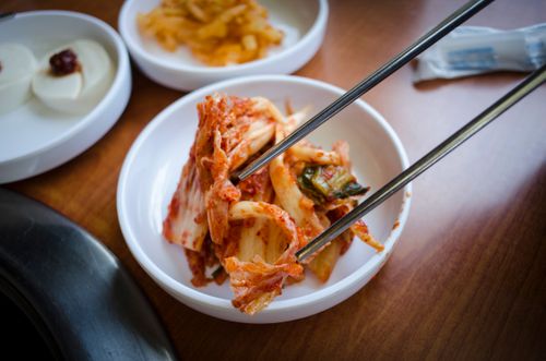 Free Close-up of traditional Korean kimchi in a ceramic bowl with chopsticks on a wooden surface. Stock Photo