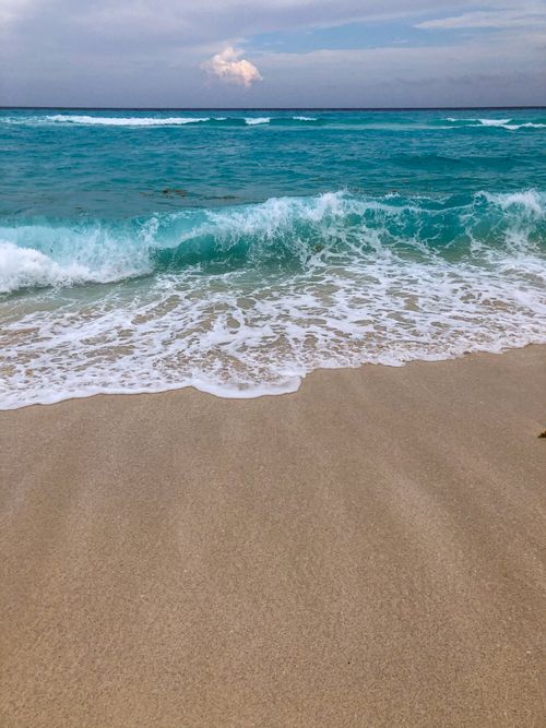 Free Serene beach view with turquoise sea waves gently hitting the white sandy shore on a calm day. Stock Photo