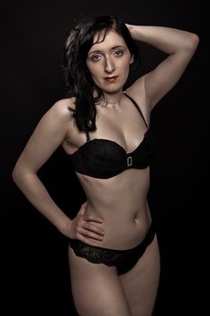 Captivating studio portrait of a woman posing in black lingerie against a dark background.