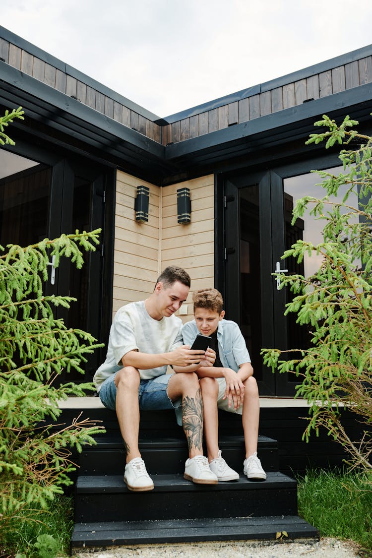 A Man And Boy Looking The Smartphone Together 