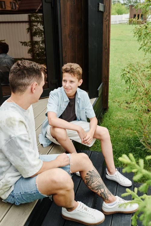 Free Two boys sitting on porch steps, engaged in conversation during a warm summer day. Stock Photo