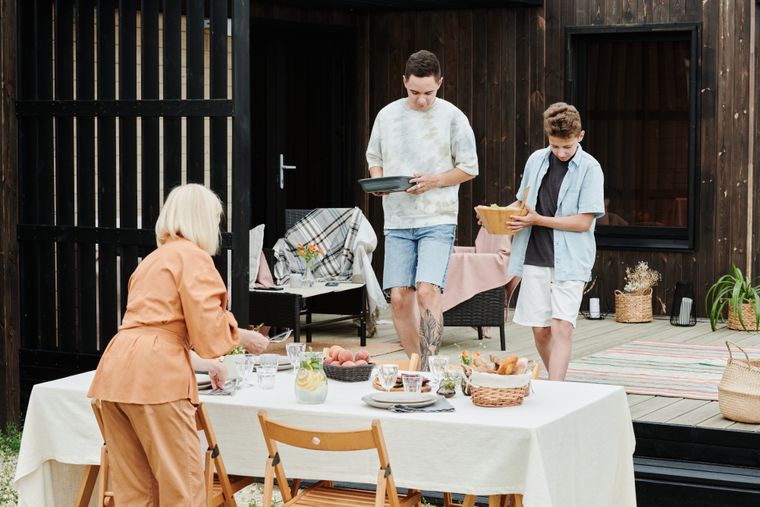 Family setting an outdoor shared table with food for a neighborhood meal. Photo by Julia M Cameron on Pexels.