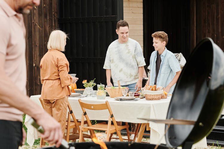 Smiling Sons Standing By Table And Mother In Yard At Barbecue