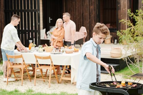 Free A boy grills food outdoors during a family gathering, perfect for summer or holiday themes. Stock Photo