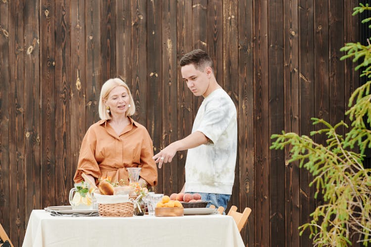 Woman And Young Man Standing In Front Of A Table With Food