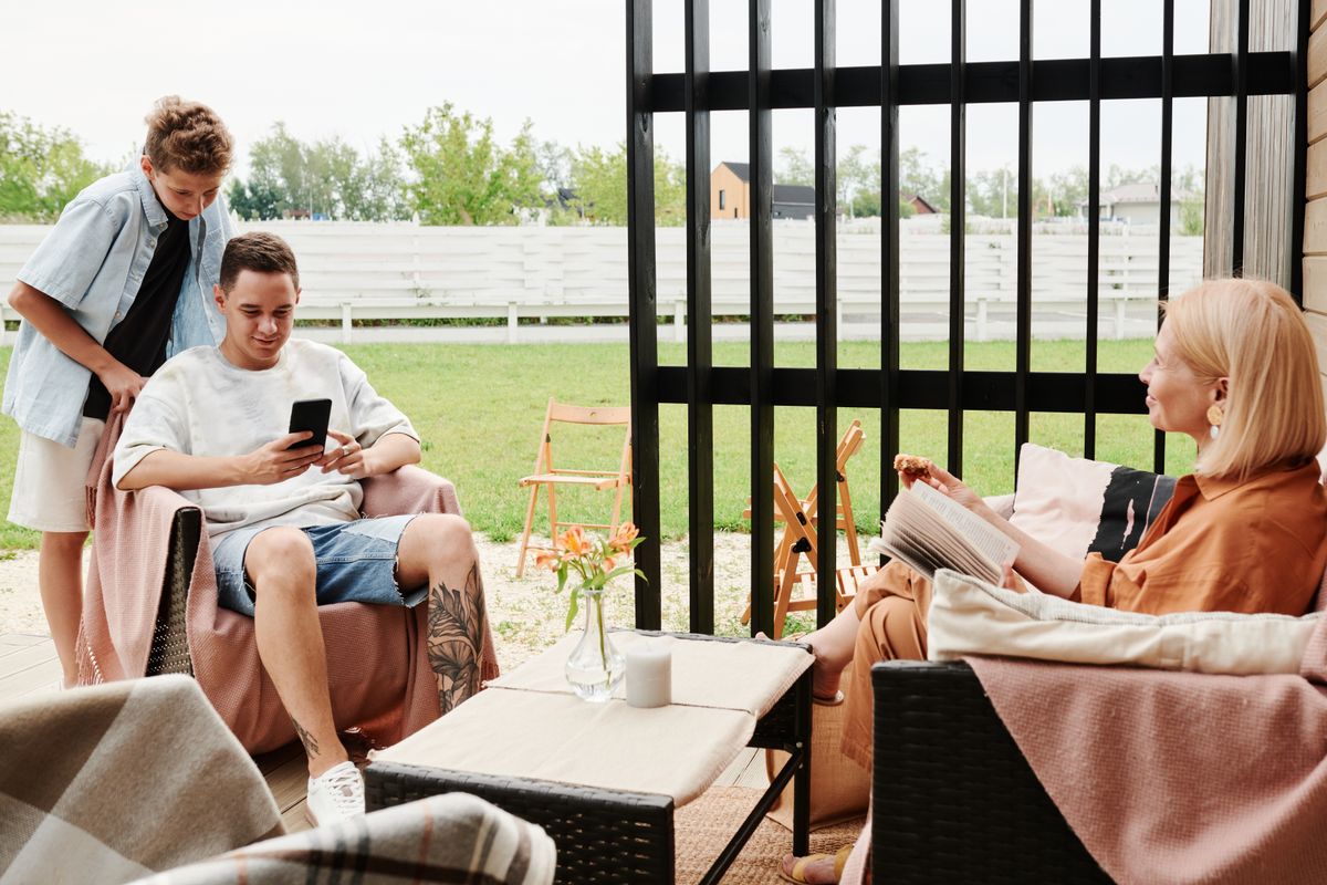 Familie sitzt entspannt auf einer überdachten Terrasse zusammen, Loungemöbel und Gartenblick