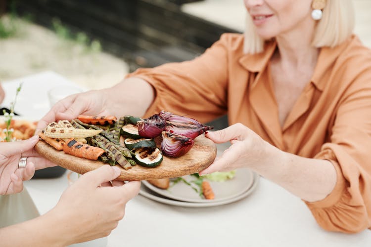 Woman Handing A Platter Of Roasted Vegetables