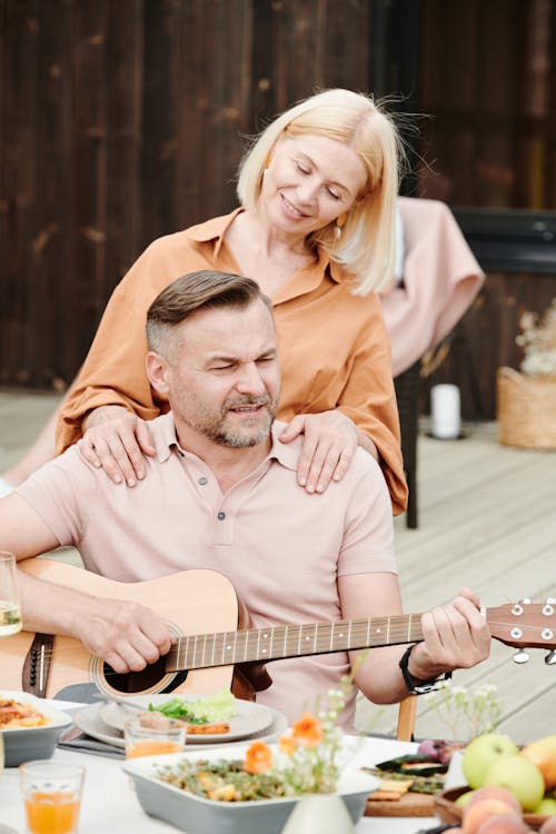 Free Man in Brown Button Up Shirt Playing Guitar Beside Woman in Brown Long Sleeve Shirt Stock Photo