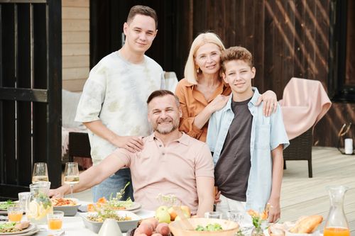Free Family of four dining outdoors in a cheerful atmosphere with a table full of food and beverages. Stock Photo