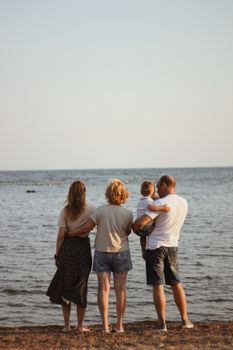 Family standing on a sandy beach, looking at the sea during a summer day.