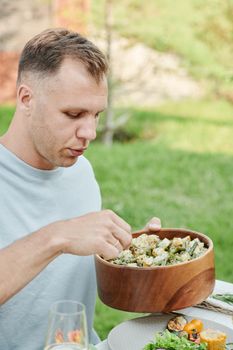 A man enjoys a fresh salad outdoors in a sunny garden setting, perfect for a healthy lifestyle theme.
