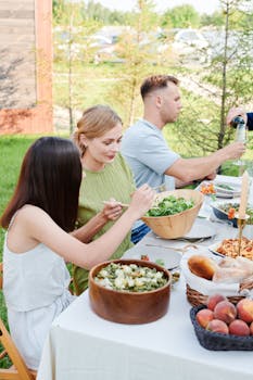 A group of friends enjoying a fresh meal outdoors during summer. Features salads, peaches, and wine.