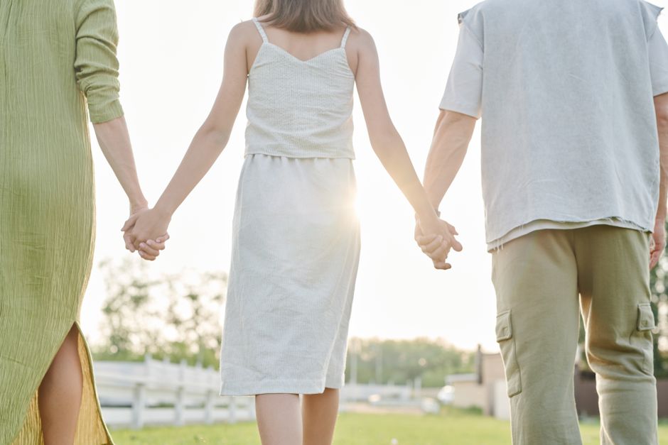Three people holding hands, walking outdoors in bright sunlight, symbolizing togetherness.