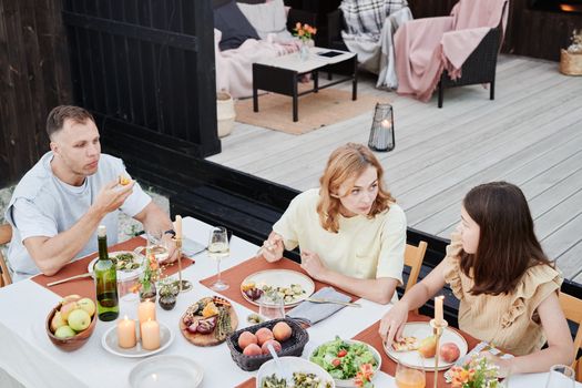 Family enjoying a meal outside with fresh food, wine, and candles creating a cozy atmosphere.