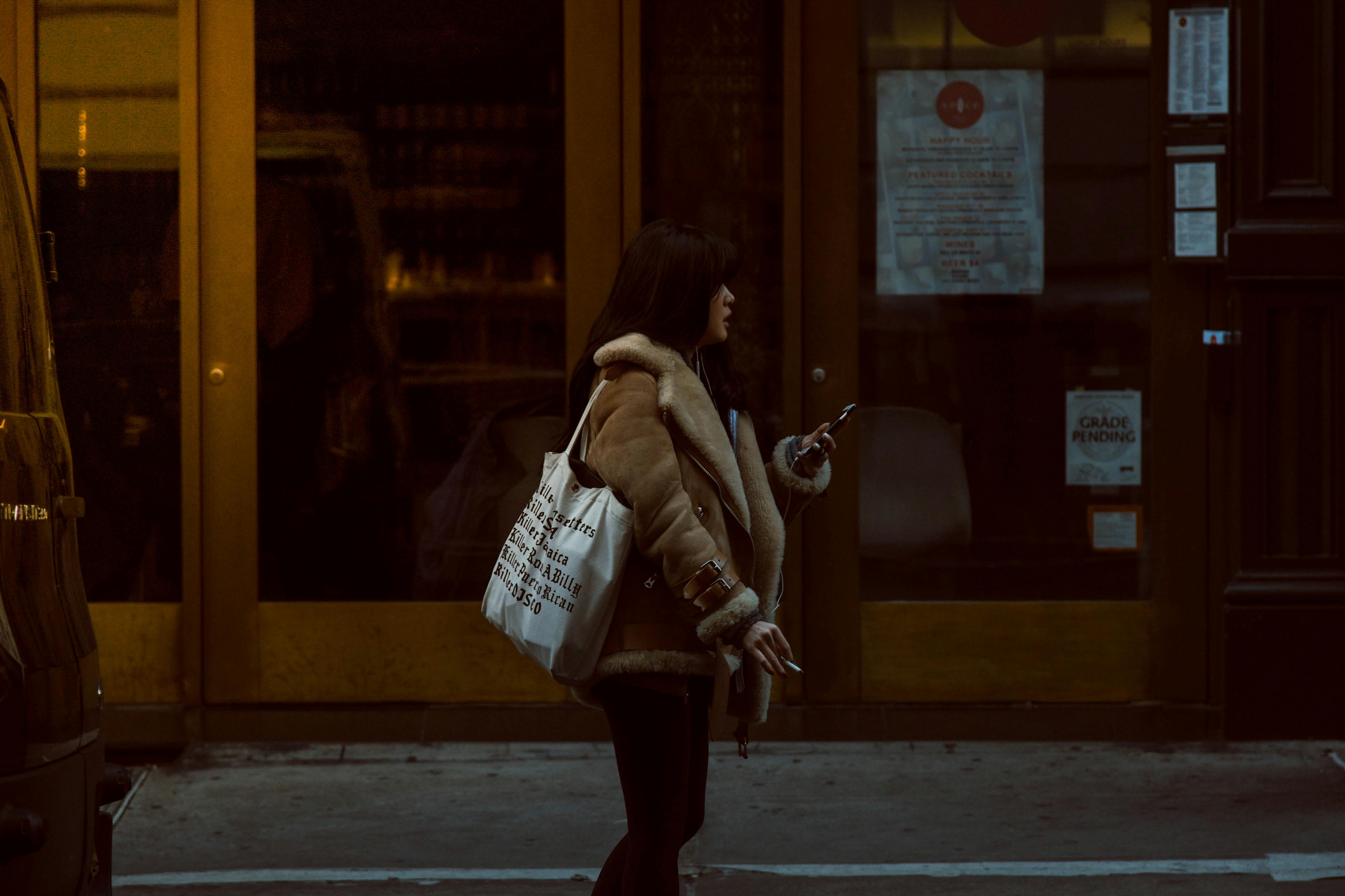 Woman Carrying White Tote Standing Beside Brown Glass Door Building