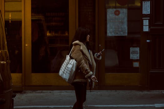 一名女子穿着冬装，手拿购物袋和智能手机，走在纽约市的街道上