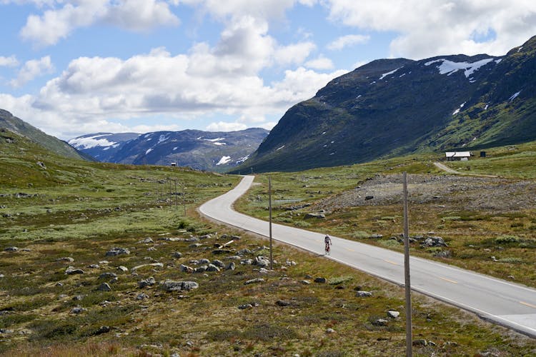 Person Cycling On A Road Between Mountains