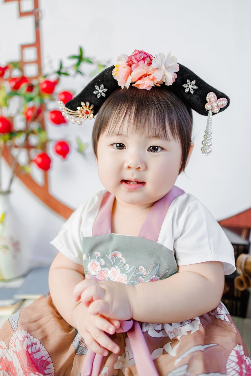Cute baby wearing traditional attire, sitting indoors with floral headpiece in Hồ Chí Minh, Vietnam.