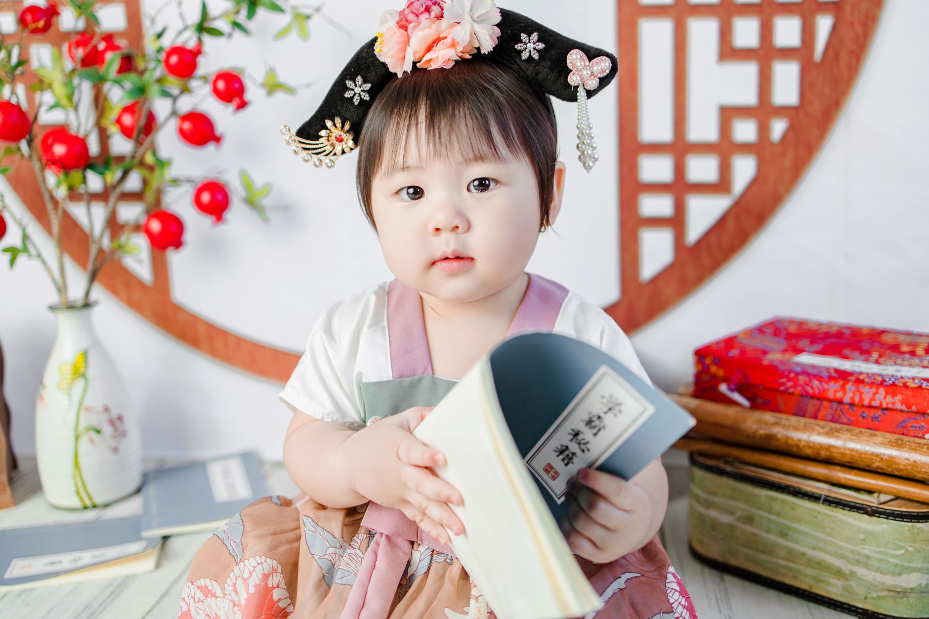 Cute baby girl in Vietnamese attire holding a book indoors, showcasing cultural heritage.