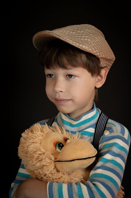 Close-Up Photo of a Boy in a Brown Flat Cap Holding His Stuffed Toy