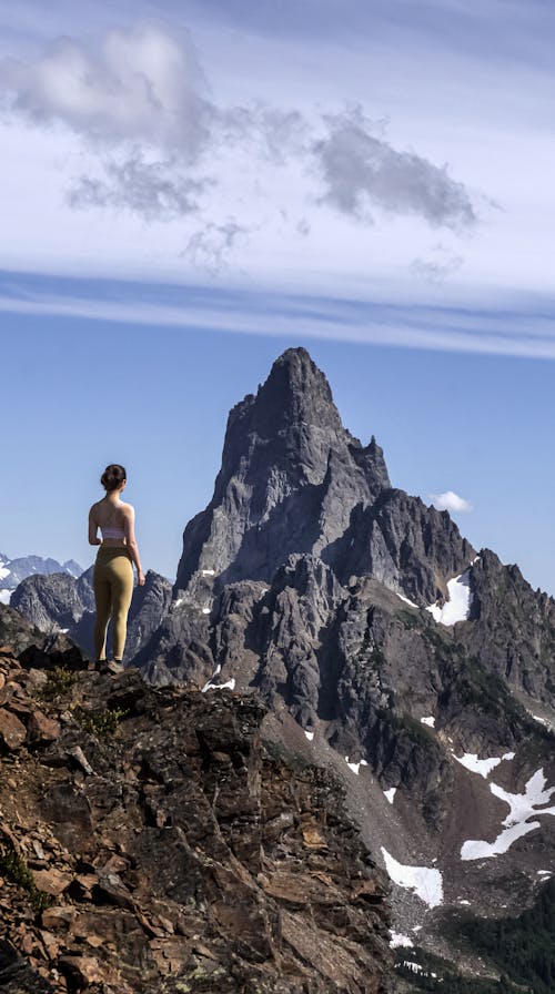 Brunette Woman on Cliff Standing and Looking at Rocky Mountain