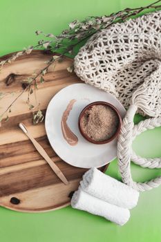 Flat lay of spa essentials including brown sugar and towels on a wooden tray with a green background.