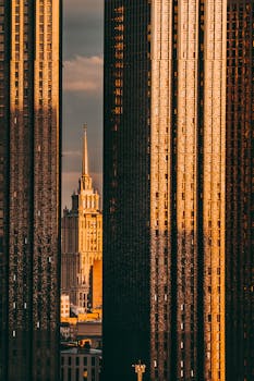 A captivating view of Moscow's architecture with a prominent spire between modern skyscrapers at sunset.