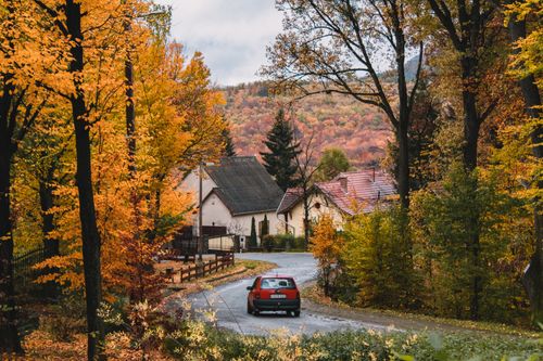 Free Charming autumn scene of a village with colorful trees and a red car on a winding road in Parádsasvár, Hungary. Stock Photo