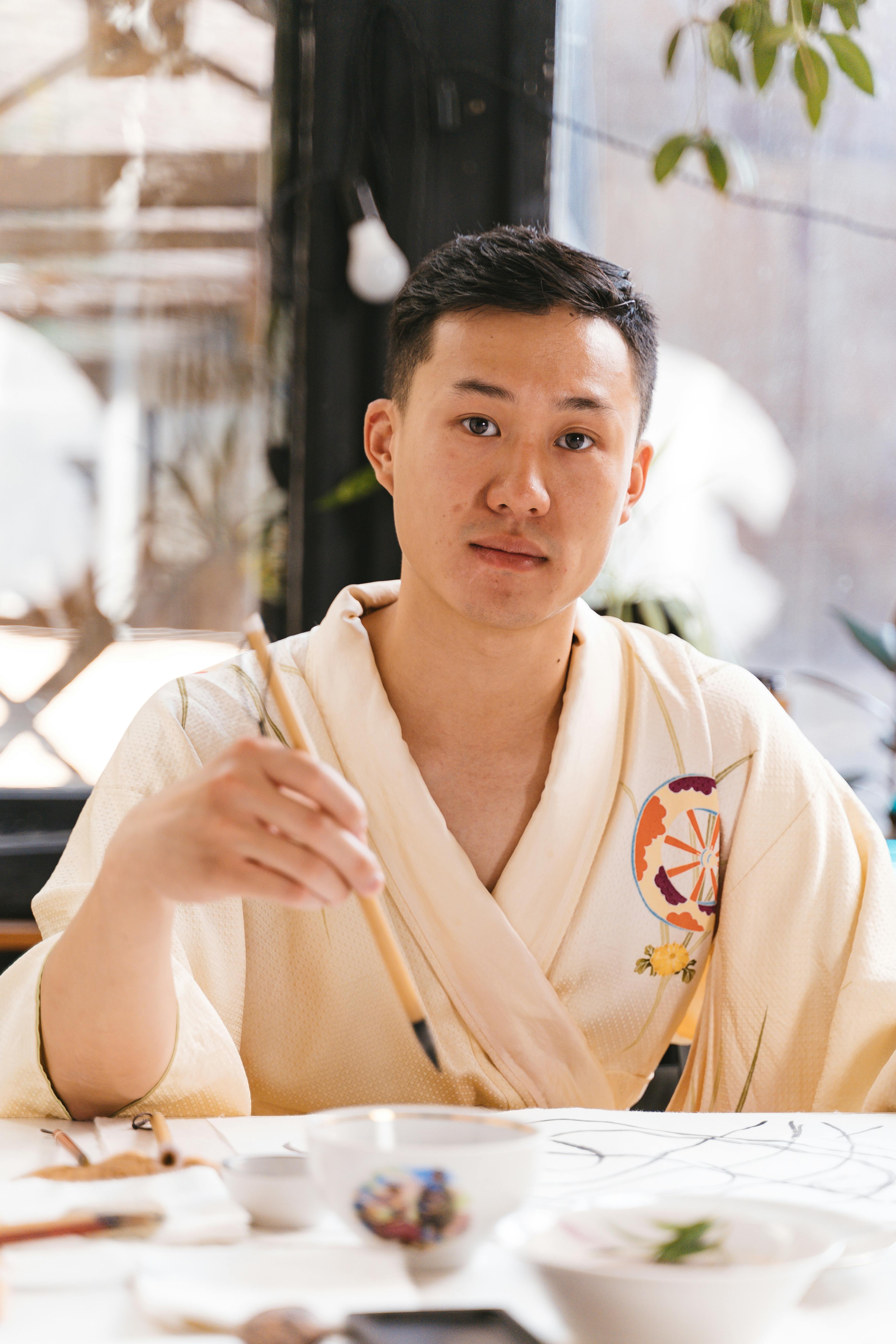 Young man engaged in Japanese calligraphy at a table, indoors, expressing artistic creativity.