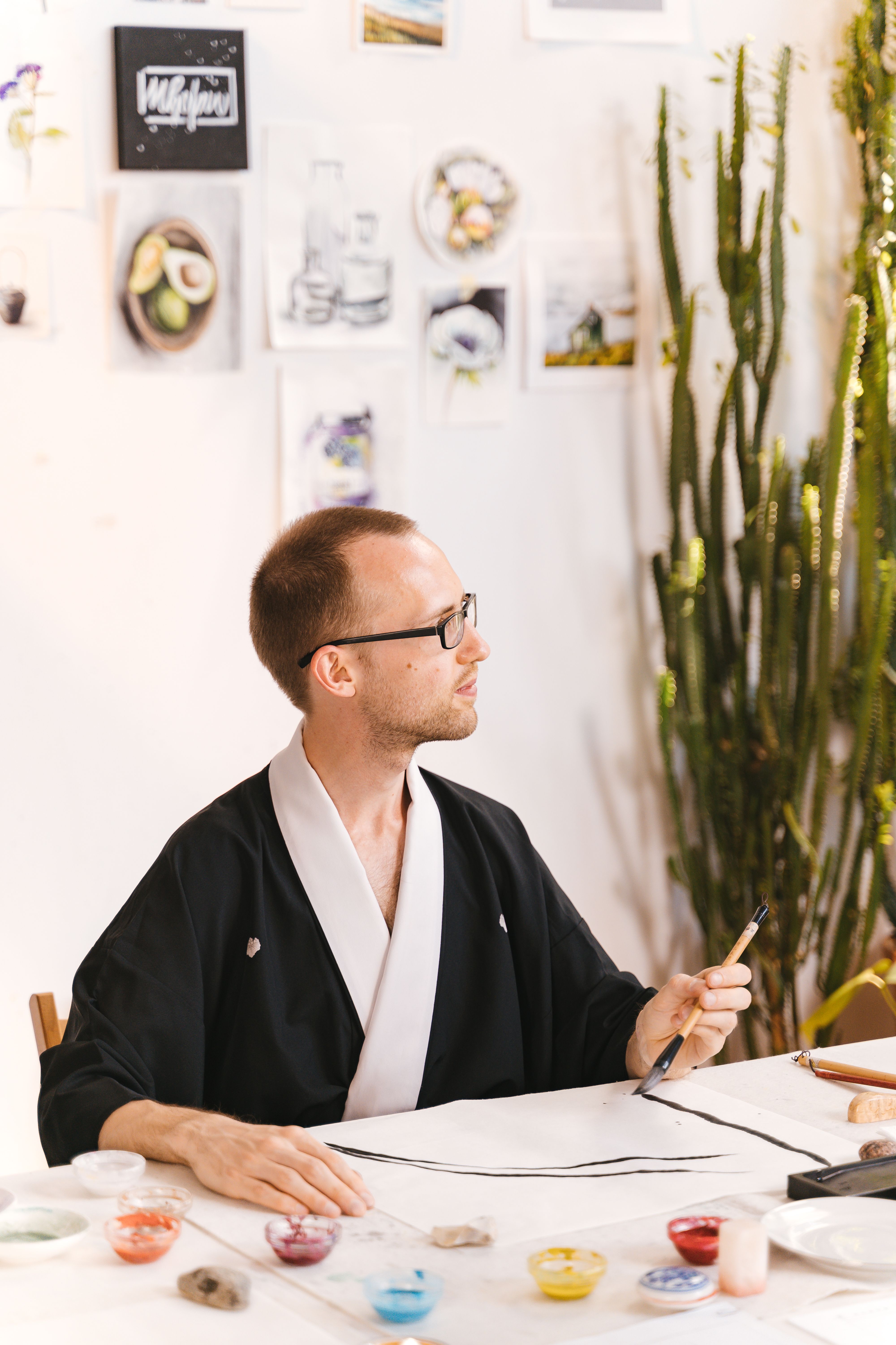 Adult male artist in a studio working on traditional Japanese painting techniques surrounded by art materials.