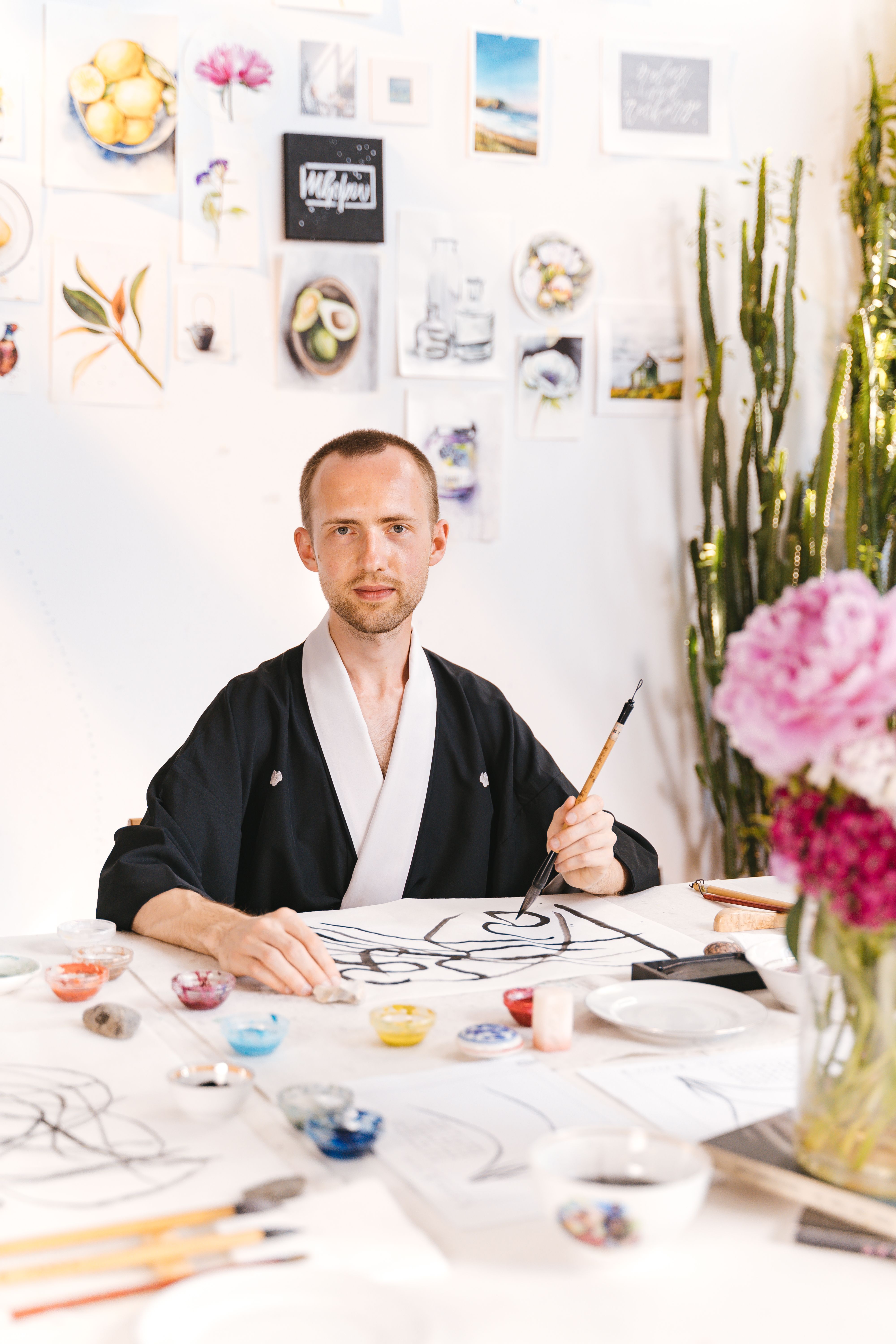 Artist focused on creating abstract art in a bright, indoor studio filled with plants and sketches.