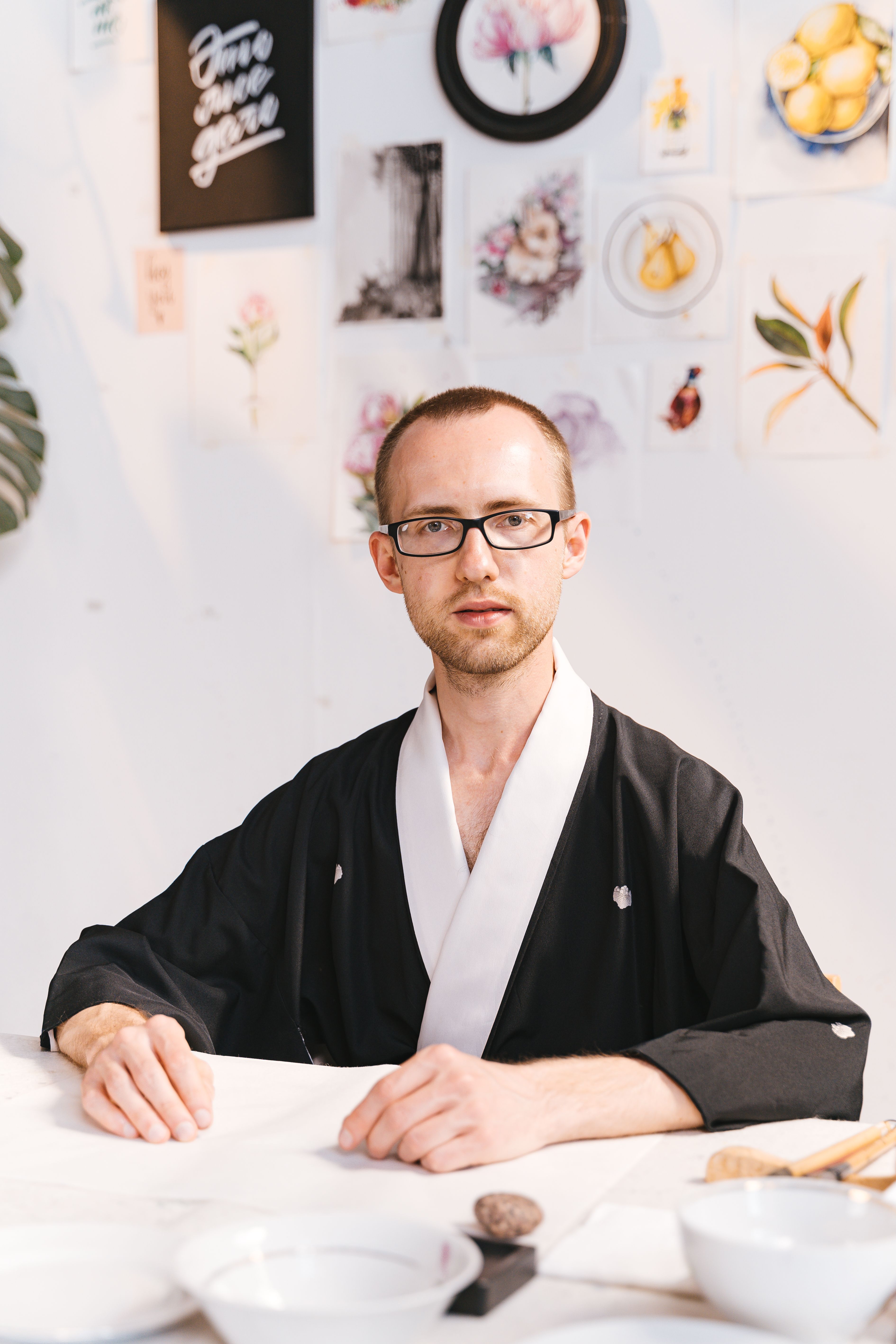 A man in a black robe sitting in an art studio, surrounded by paintings.