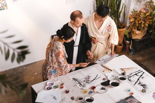 Three adults engaged in a creative ink painting session, focusing on traditional techniques.
