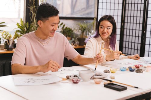 Free Young adults in an indoor creative workshop using brushes and colors, smiling and collaborating. Stock Photo