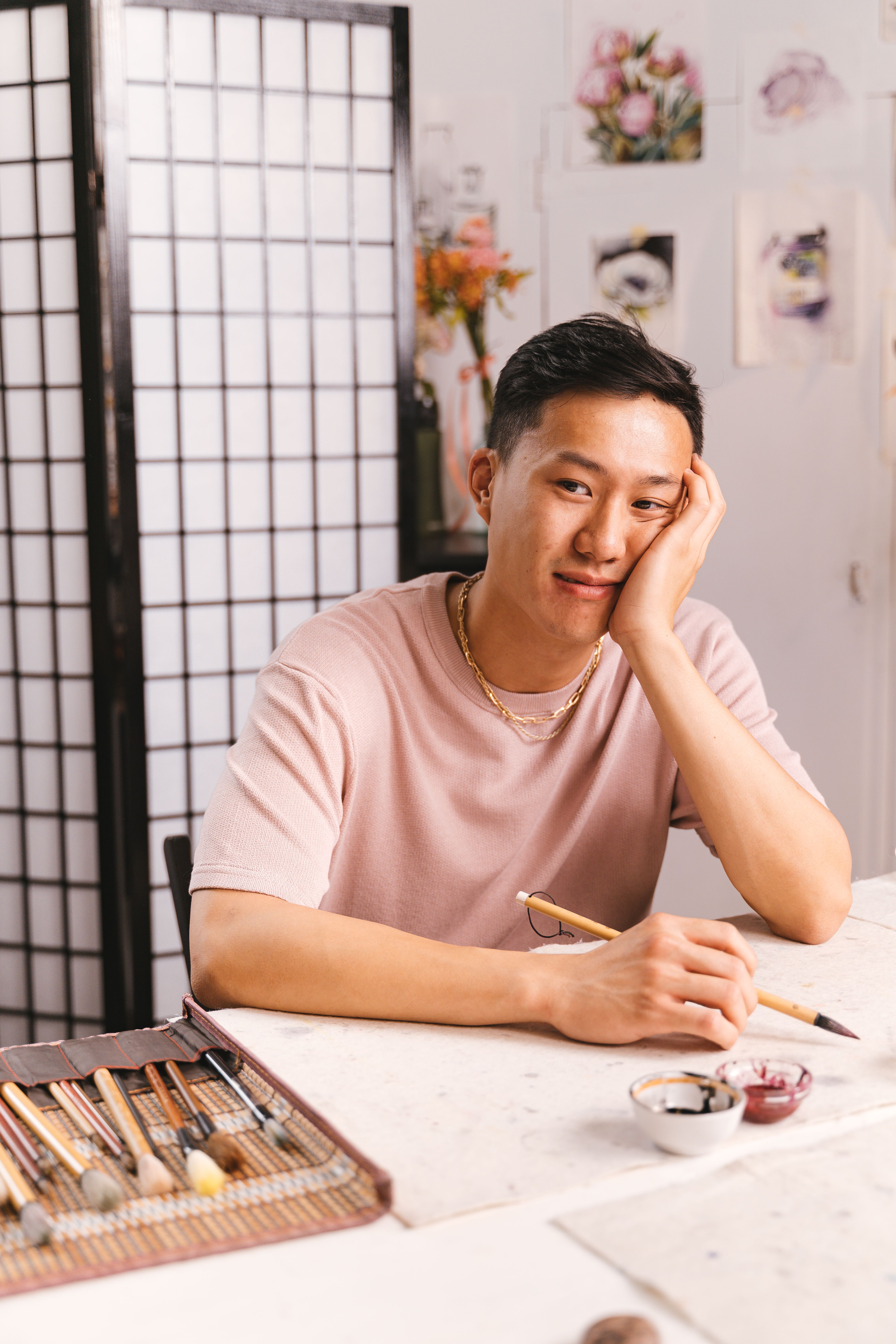 Young artist with paintbrush seated indoors, contemplating creativity.
