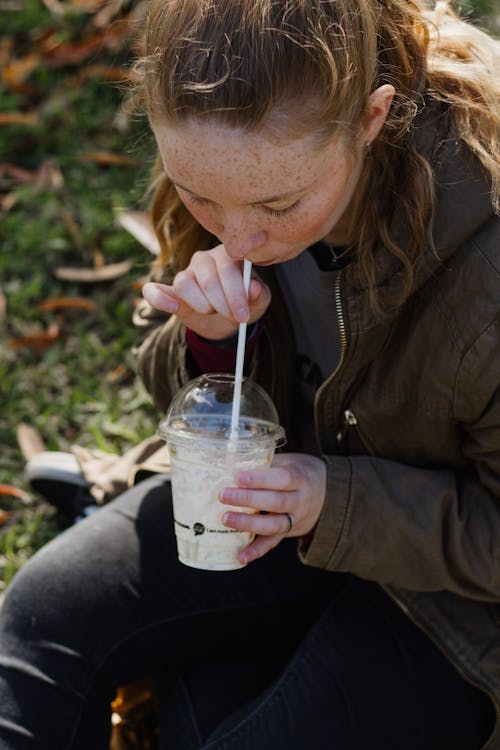 Free Woman in Brown Leather Jacket Sipping on Clear Plastic Cup Stock Photo