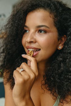 A woman with curly hair enjoys a healthy snack indoors, promoting wellness and nutrition.