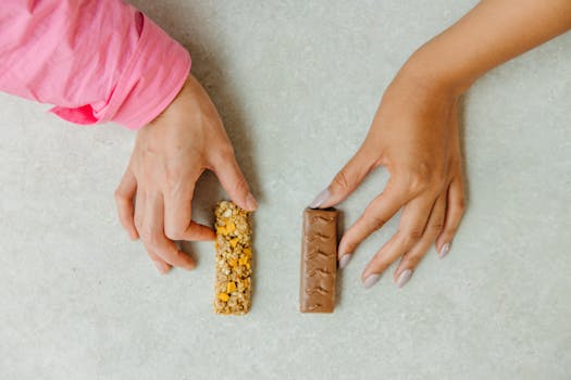 Two hands holding a chocolate bar and a granola bar, showcasing a snack choice concept.
