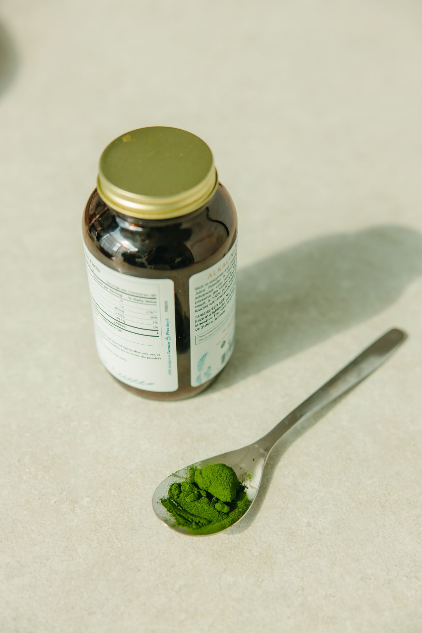 Green herbal supplement powder beside a container on a neutral surface