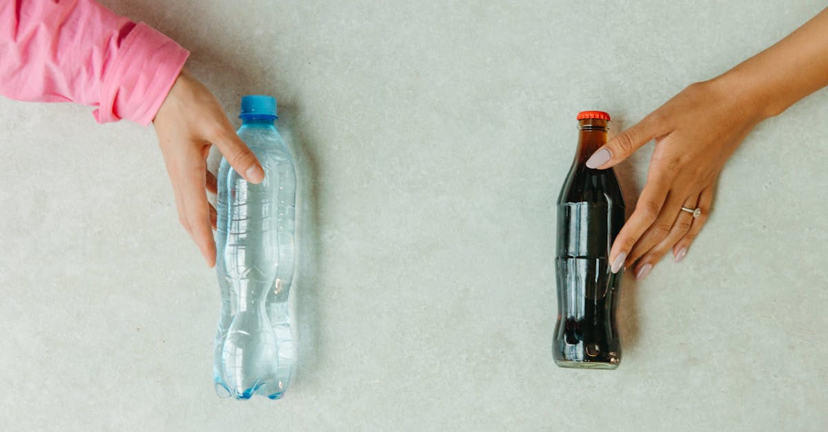 Close-up of hands reaching for a bottled water and a soda bottle on a light surface. Close-up of hands reaching for a bottled water and a soda bottle on a light surface.