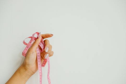 A woman's hand holds a pink measuring tape against a plain background, offering ample copy space.