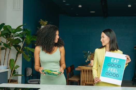 Two women discussing healthy eating with a sign and vegetables.